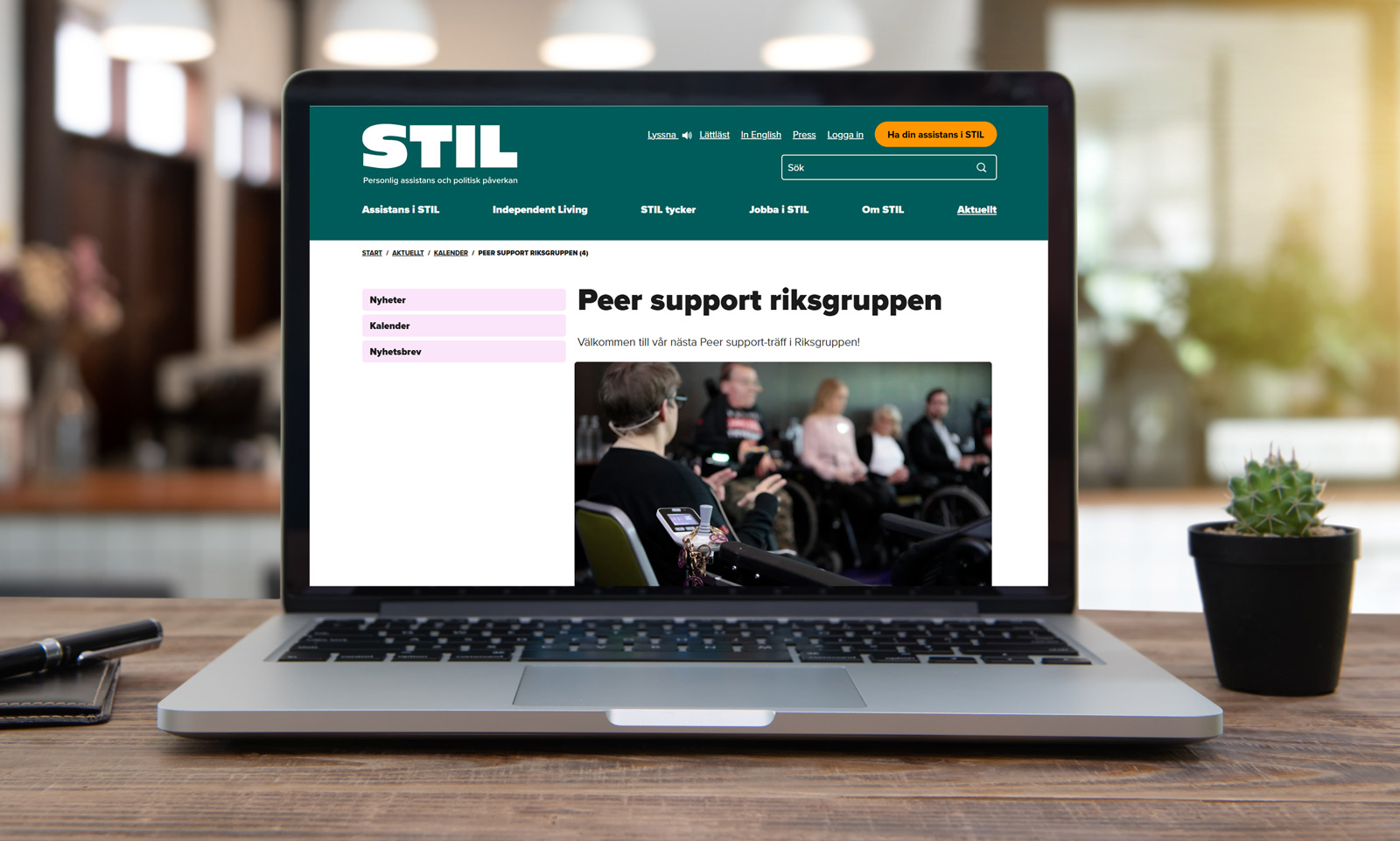 Laptop som visar STILs nya webbplats med Peer support-sidan, i en hemmiljö med växt och anteckningsbok