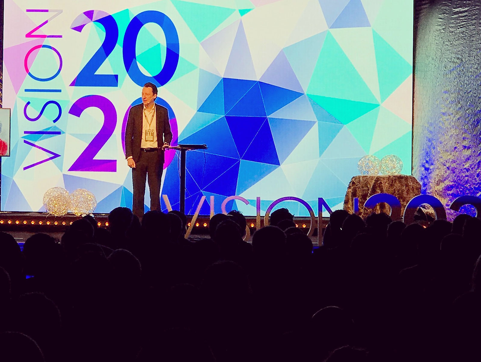 Talare på scen framför Vision 2020-bakgrunden under konferensen